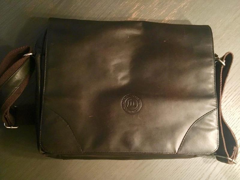 The closed brown leather messenger bag sitting on a wooden table
