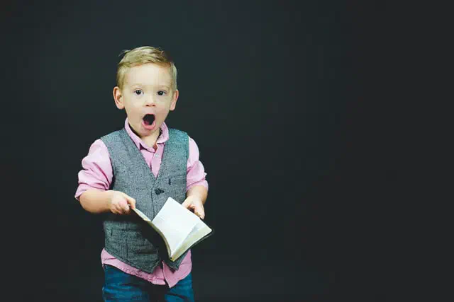 Young boy in a vest looking surprised while holding an open book