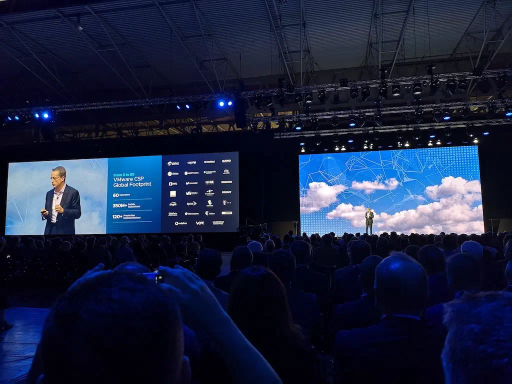 VMworld keynote stage with a speaker and screens listing partner logos including Proact